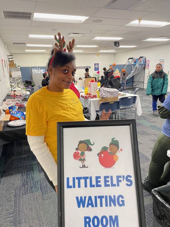 A volunteer welcomes kids to a waiting room while parents and guardians shops for gifts.