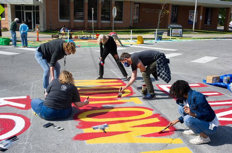 Community members watch as artists and volunteers paint a 'Luv Midtown KC' mural in the middle of anintersection in Kansas City, Missouri.