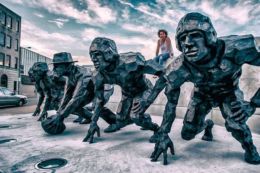 Artist Gail Folwell sits behind her bronze sculpture of the NFL Draft, the second greatest moment in professional football.
