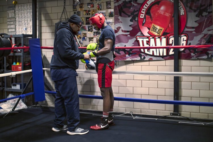 Coach Fred helps his 25-year-old son, "Dynomite" Fred Wilson Jr., with his gloves before a sparring match with a boxer from Akron.