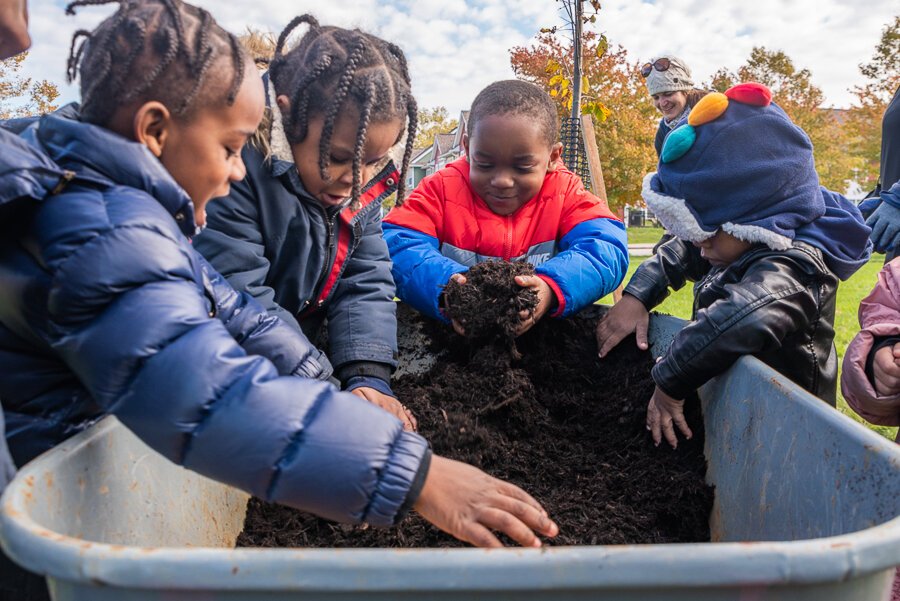 Local children helping with mulching a tree after planting at Carver Park Estates on Unwin Road.