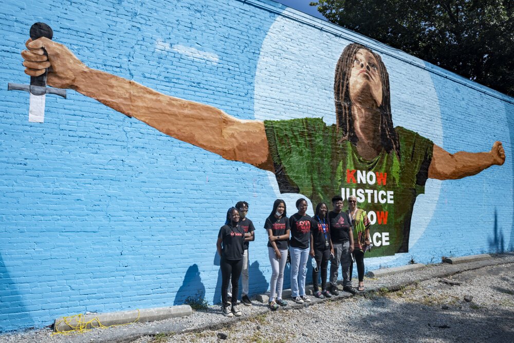 Artist Robin Robinson (right) poses with staff of Cleveland UMADAOP by her mural painted with artist Gary Williams at 1215 E. 79th Street.