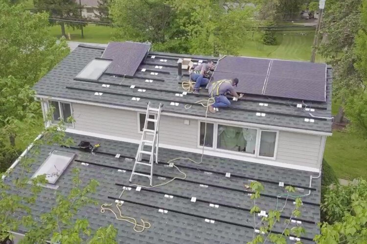 Workers install solar panels to the roof of a residential home.