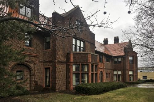 On the exterior, The Drury house boasts a red brick façade with recessed arches, bay windows, orange slate roof, dark chimney, and a brick tower.